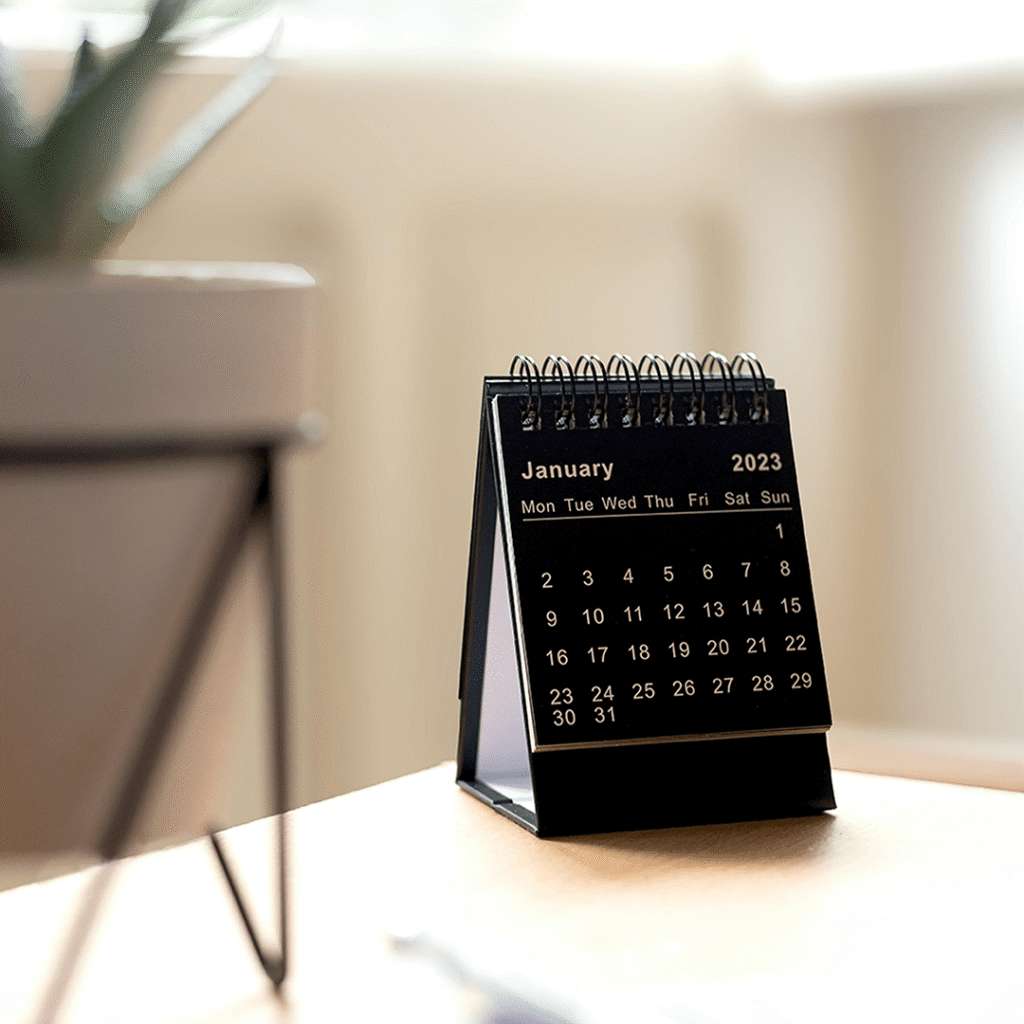 A desk calendar with a small green plant beside it, showcasing a blend of organization and nature in a workspace.