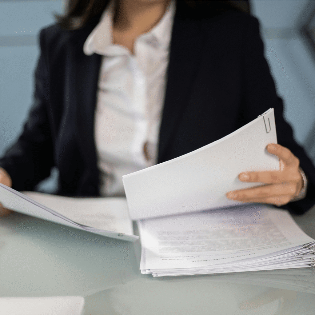 A woman in a business suit holds papers, appearing focused and engaged in her work environment.