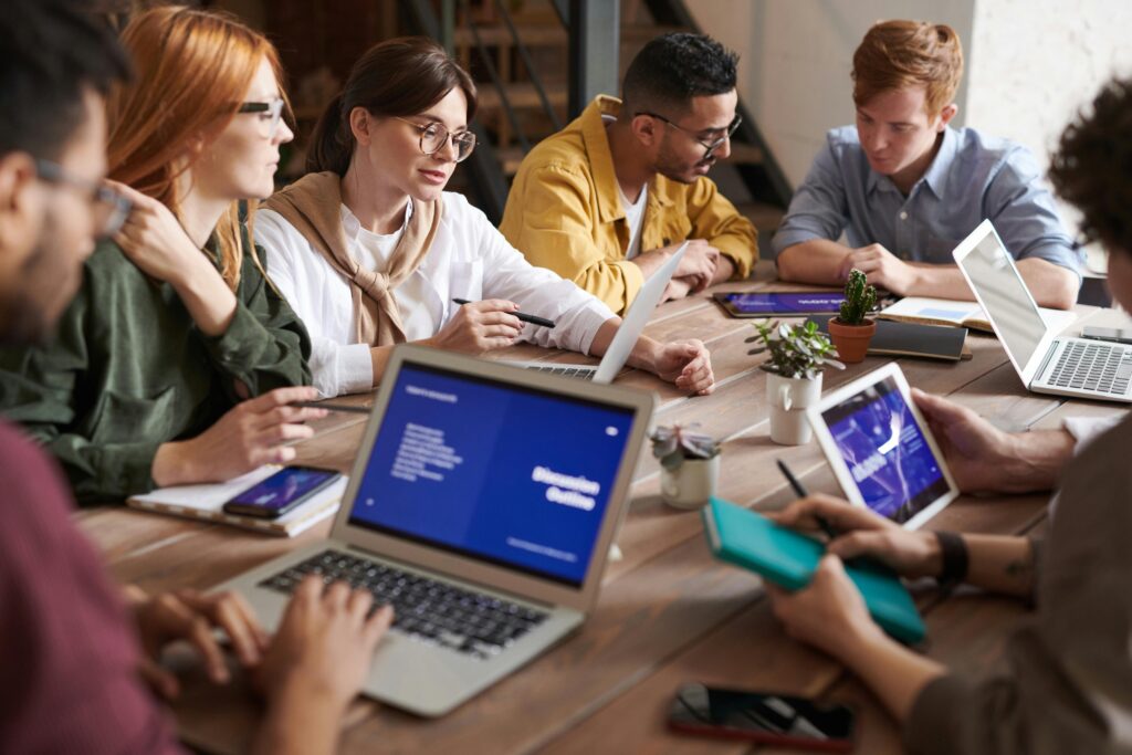 A diverse group of people collaborating around a table, each using a laptop for discussion and teamwork.